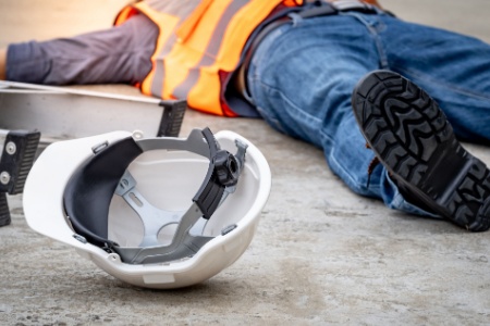 An injured construction worker lying on the concrete after a fall from a ladder, illustrating a workplace construction accident.