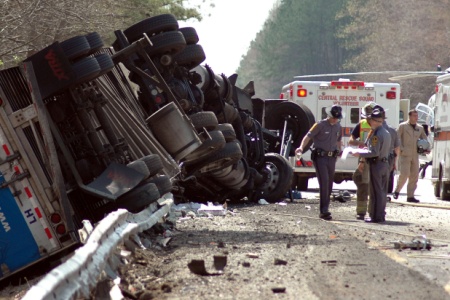 Accident scene showing an overturned tractor-trailer on its side, with police officers, a Central Rescue Squad ambulance, and a helicopter in the background.